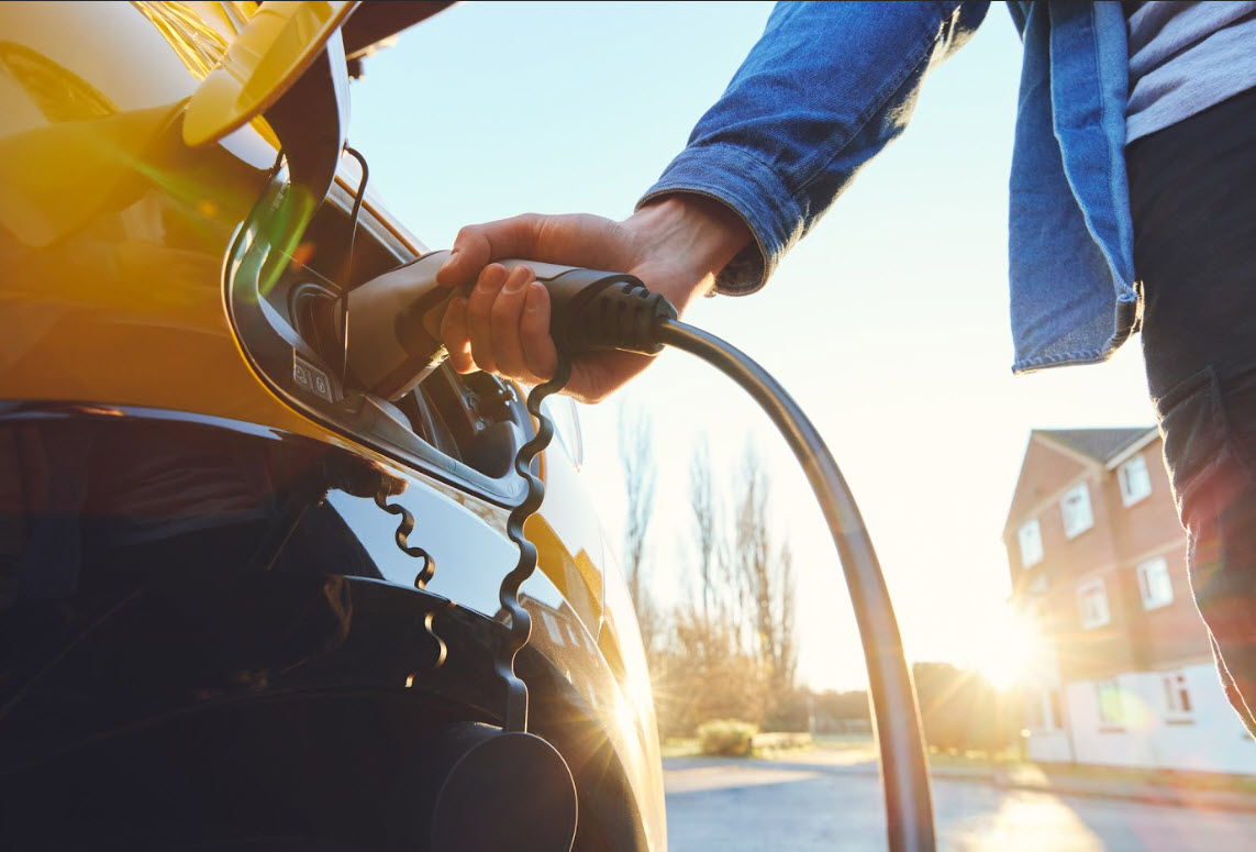 A man charges his yellow electric vehicle on a fall day