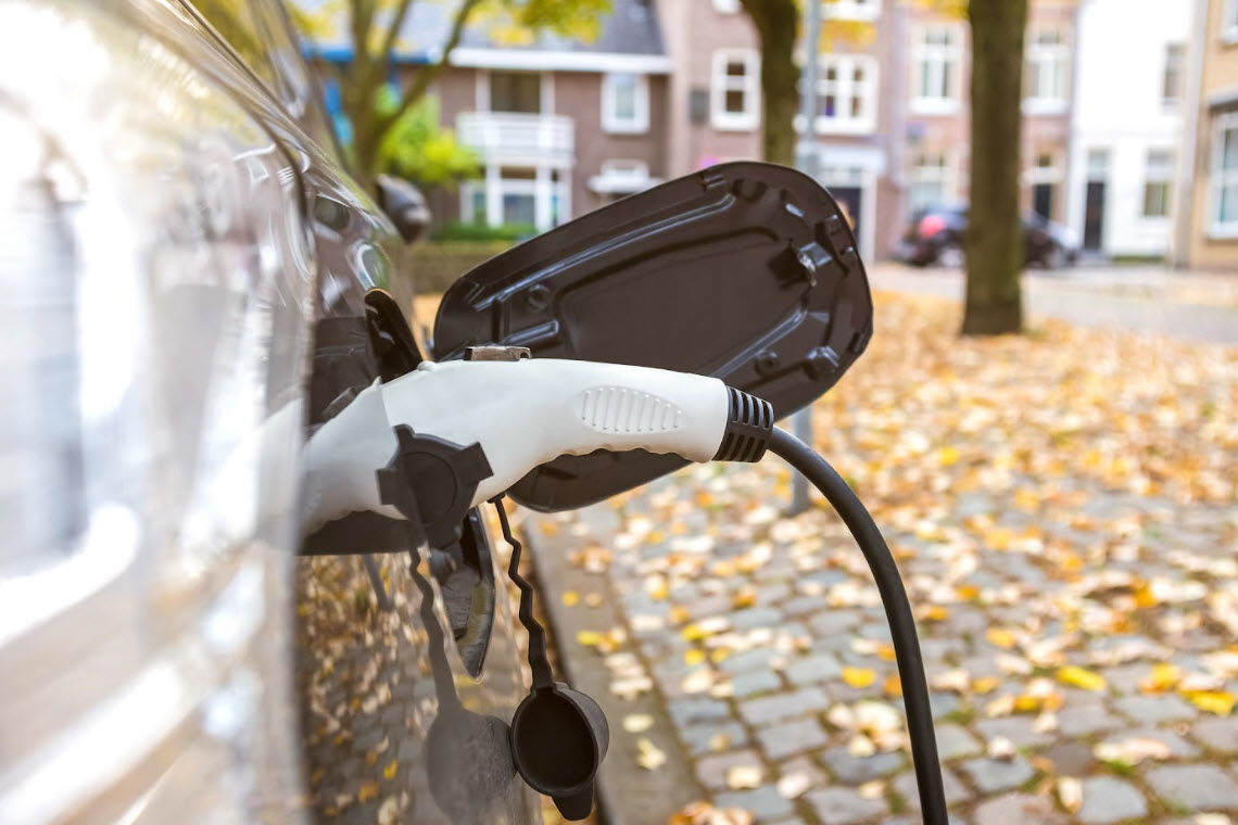 A plug charges an electric vehicle on a residential street in Autumn