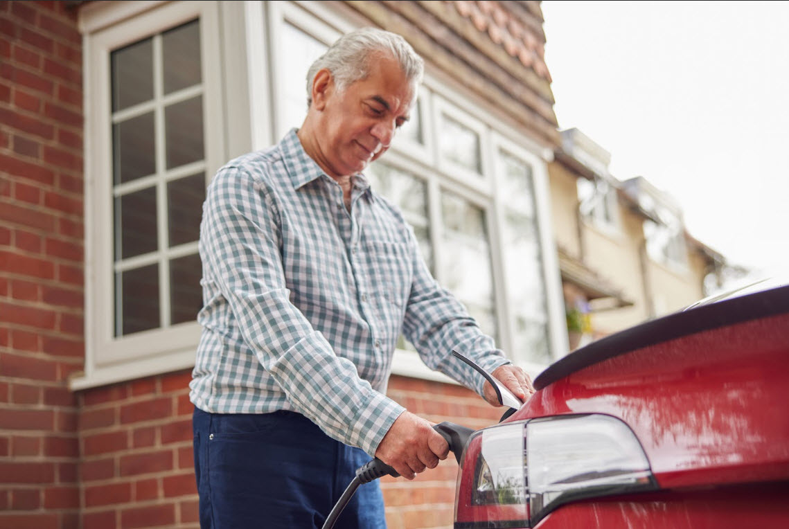 An older gentleman plugs in his electric vehicle outside his house