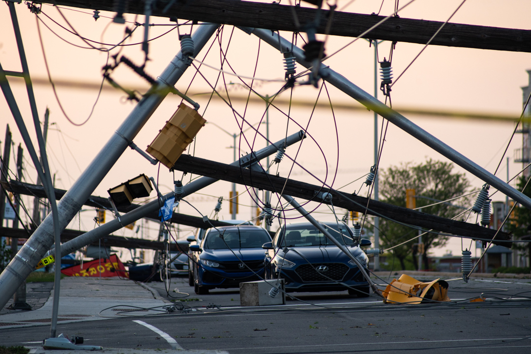 Multiple hydro poles, wires and streetlights lay broken on a road after a storm