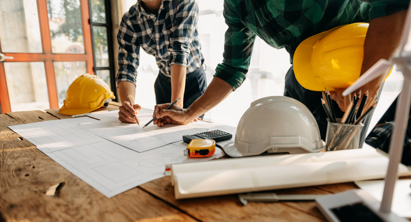 Contractors carrying hard hat and marking up blueprints on a construction site