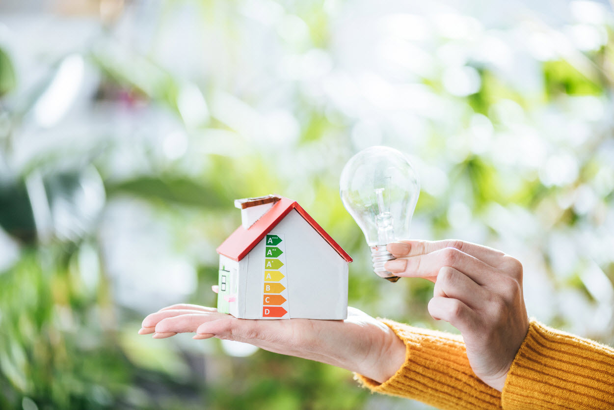 A woman holds a small house with a light bulb beside it