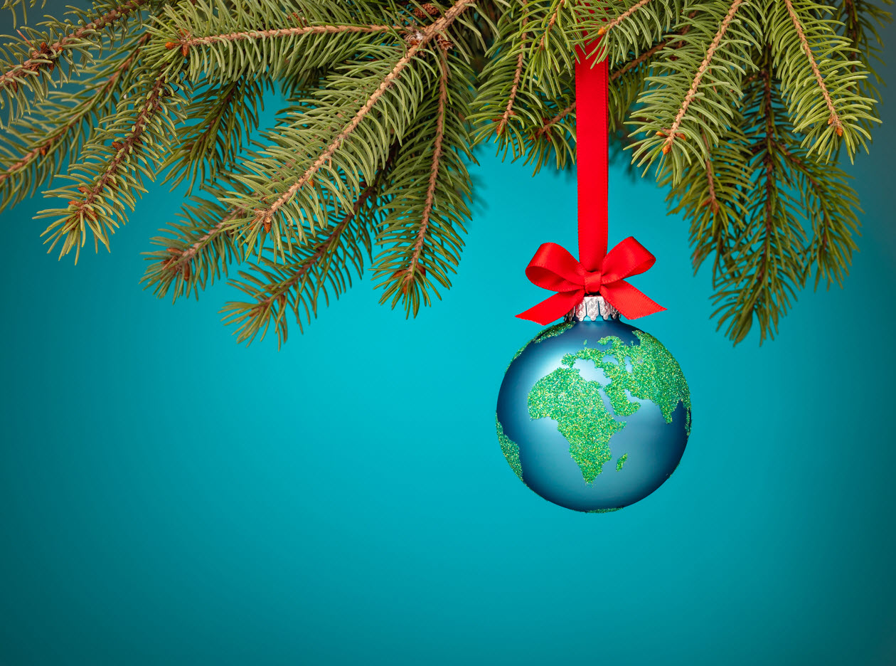 An ornament of the world hanging from a red ribbon on a Christmas tree