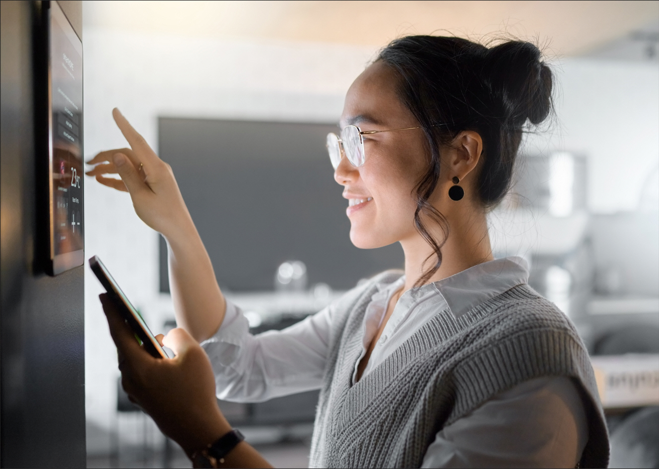 A woman controls her smart thermostat and uses a smart phone