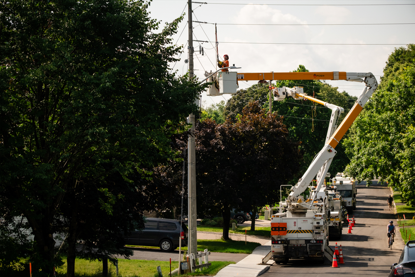 A cyclist and pedestrian pass by hydro workers in trucks working on poles