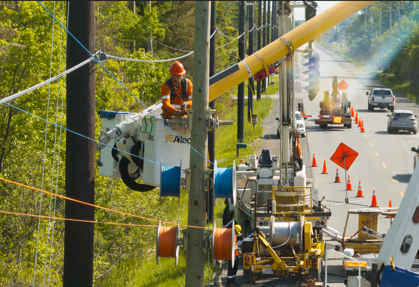 A hydro worker in a bucket works on a hydro pole while below a safety perimetre keeps traffic flowing
