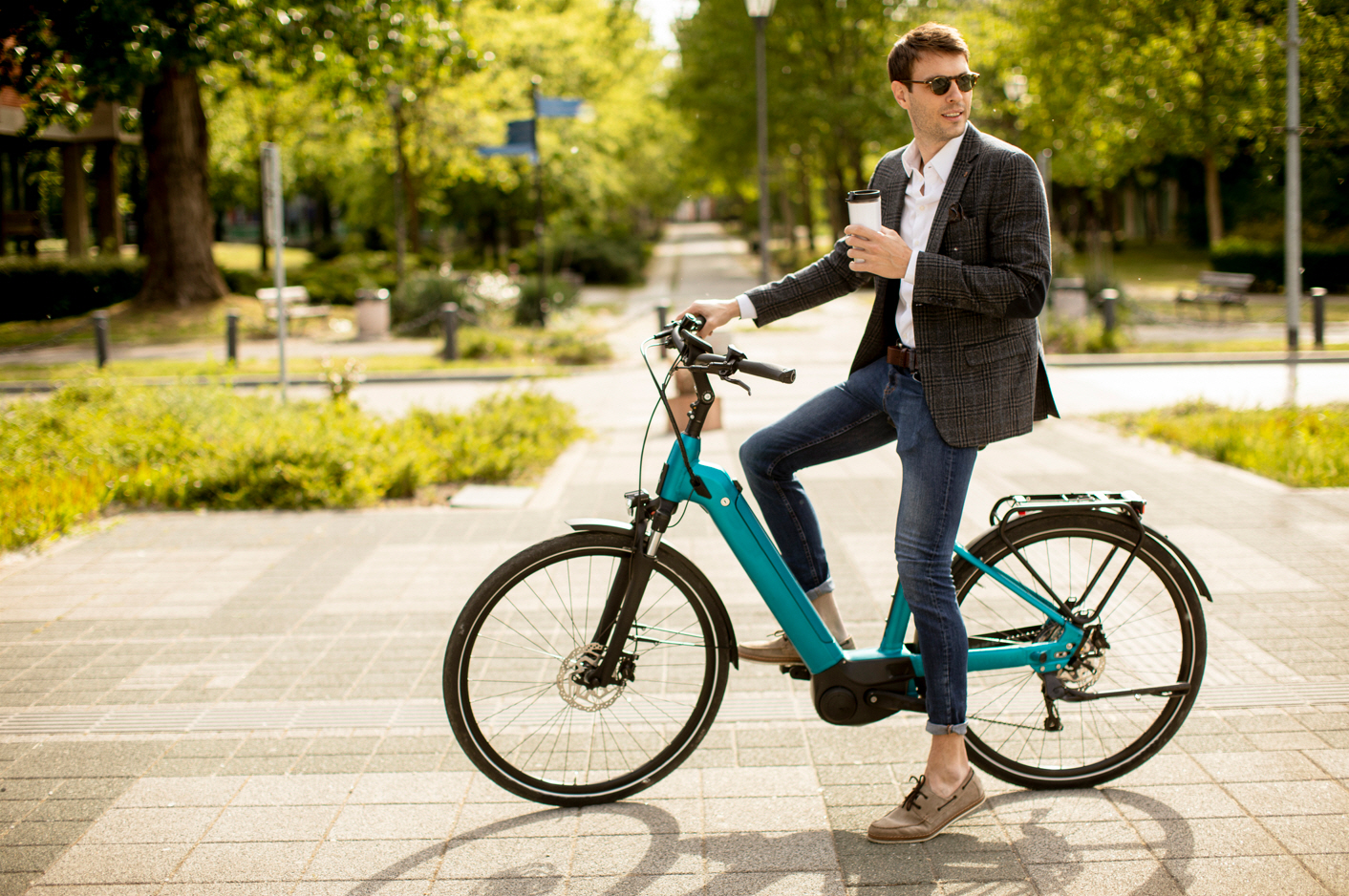 A young man on an electric bike holding a coffee