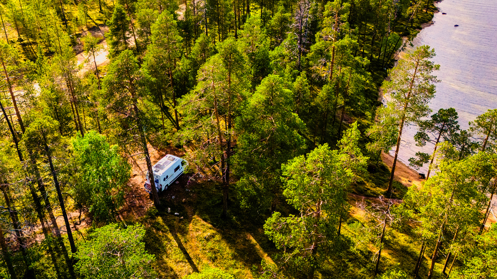 An aerial image of a camper van in the woods near a lake