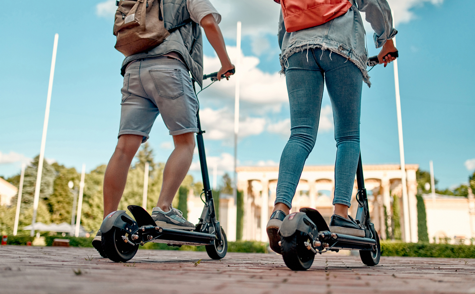 The backs of a young man and woman with backpacks on electric scooters