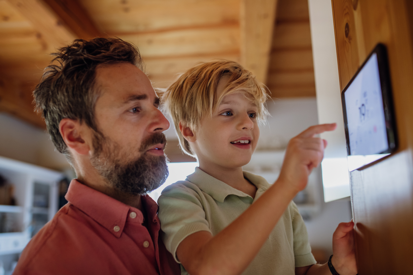 A father lifts his son up to help program a thermostat