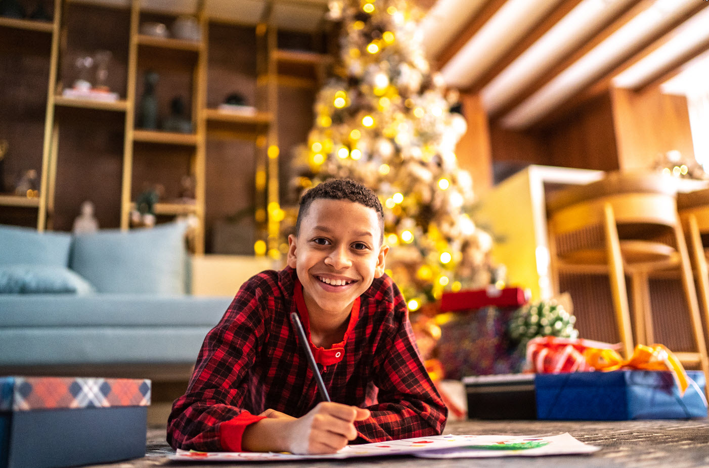 A boy in pajamas colours on the floor in front of a Christmas tree