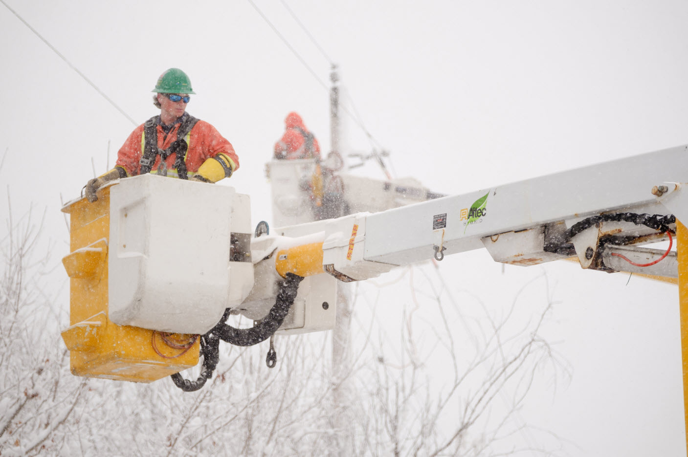 Hydro Ottawa crews carried in boom trucks close to wires, work in a winter snowstorm
