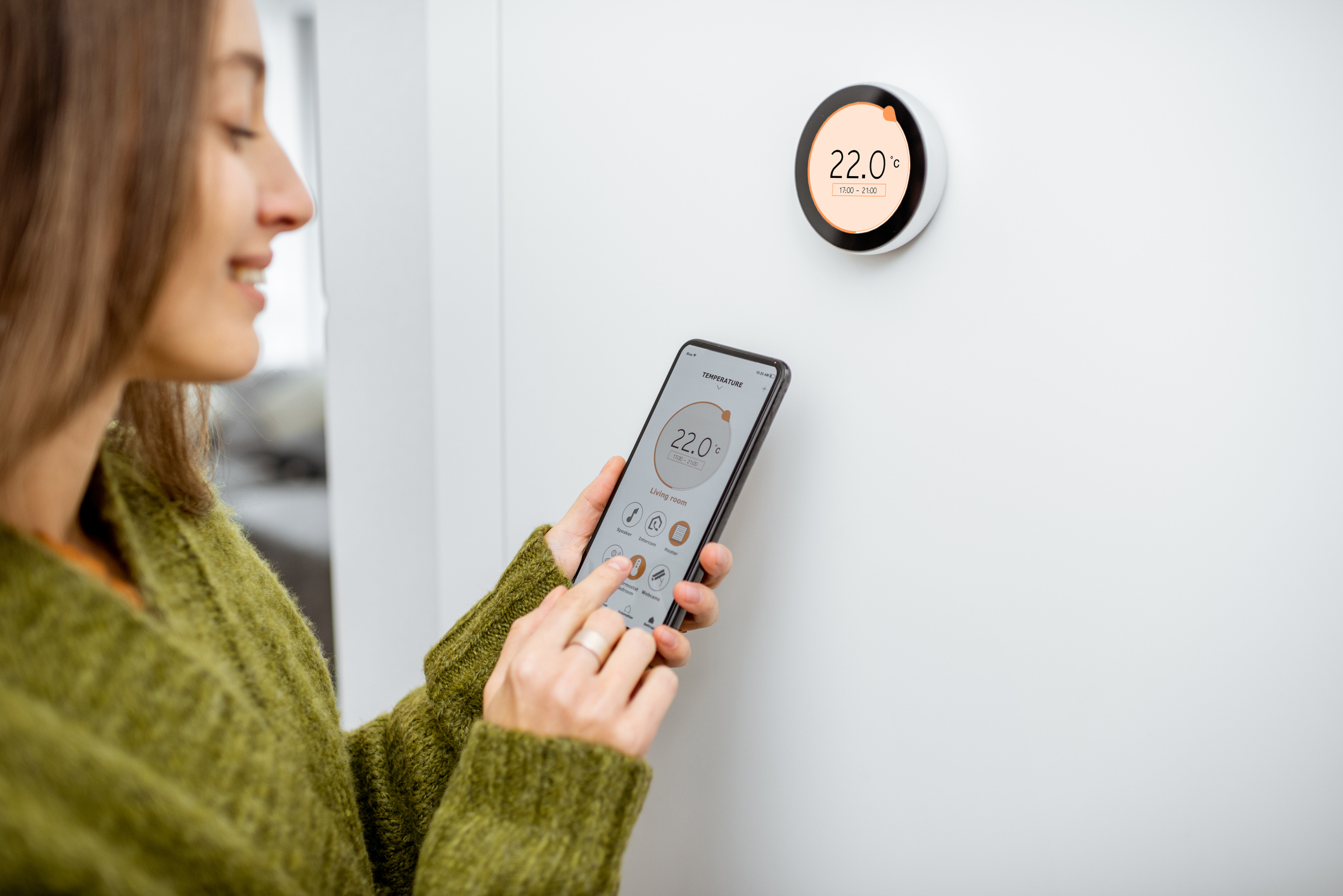 A woman interacting with a smart thermostat using her mobile device.