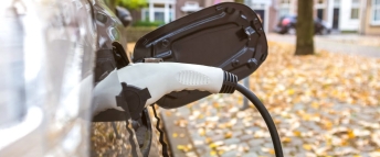 A plug charges an electric vehicle on a residential street in Autumn