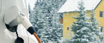 A yellow country house surrounded by trees in winter with a white electric vehicle charging in the foreground