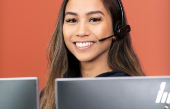 Young woman with a headset on, computer monitors in foreground