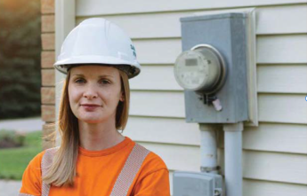 Lana Norton wears a hard hat and stands beside a meter