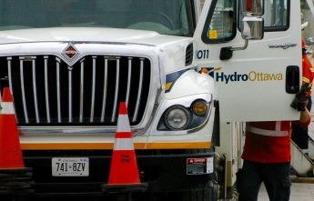 A worker holds the door open to a bucket truck with the Hydro Ottawa logo on it