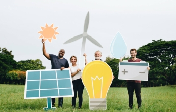 Four people hold up cardboard signs such as the sun, a wind turbine, solar panel, light bulb and battery