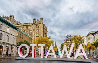 A sign spells out Ottawa with Parliament in the background 