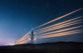 Transmission towers with glowing yellow powerlines on a starry night