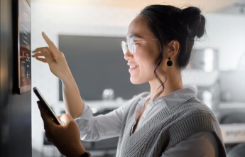 A woman controls her smart thermostat and uses a smart phone
