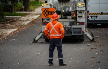 A hydro worker stands on the road surveying a worksite with vehicles and equipment