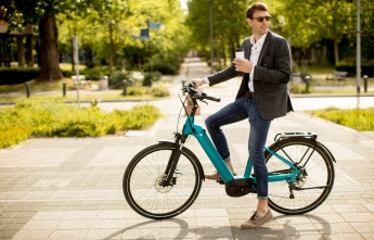 A young man on an electric bike holding a coffee