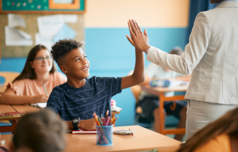 A young boy high-fives his teacher in class