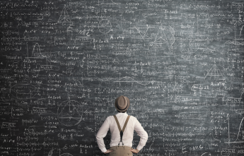 A man wearing a hat and suspenders looks at a blackboard covered in complex mathematical formulas