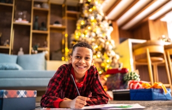 A boy in pajamas colours on the floor in front of a Christmas tree