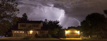 Houses lit by an approaching lighting storm.