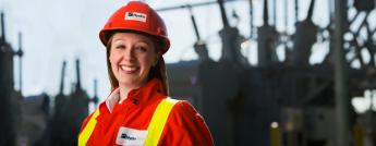  A female engineer dressed in personal protective  clothing with a transformer station in the background