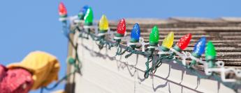 A person hanging Christmas lights on the roof of their home.