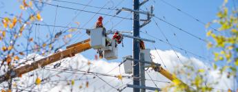 Powerline workers suspended in a bucket truck attend to a hydro pole