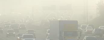 Cars and trucks drive on a busy highway covered with smog