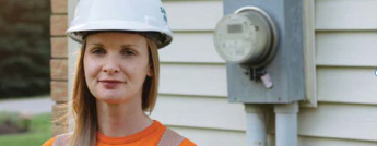 Lana Norton wears a hard hat and stands beside a meter