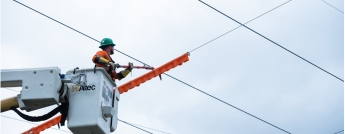 A hydro worker in a bucket working on hydro lines criss-crossing in the sky