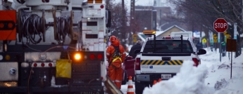 Hydro crews work on a busy snowy street with their truck lights flashing