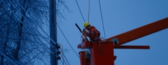 A hydro worker in a bucket approaches wires covered with ice