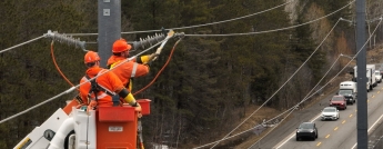 Hydro crews working high above a highway with a line of vehicles below