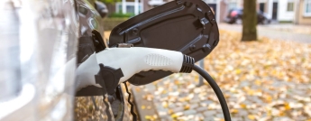 A plug charges an electric vehicle on a residential street in Autumn