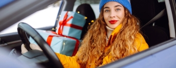 A woman behind the wheel of a car with presents in the passenger seat