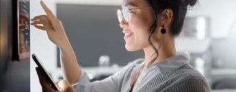 A woman controls her smart thermostat and uses a smart phone