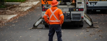 A hydro worker stands on the road surveying a worksite with vehicles and equipment