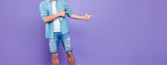 A young man in jean shorts poses with both hands pointing to the right