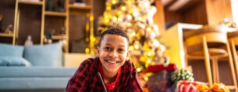 A boy in pajamas colours on the floor in front of a Christmas tree